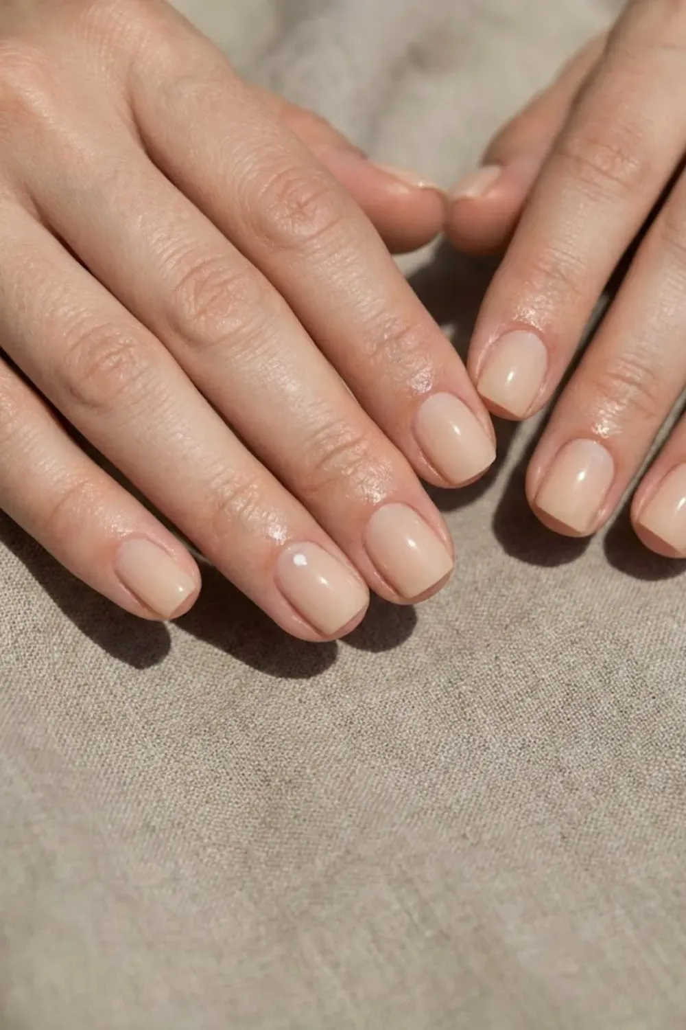 classic-solid-nude-nails-manicure  - Close-up of short, neatly shaped nails painted in a soft nude beige color, minimal aesthetic.