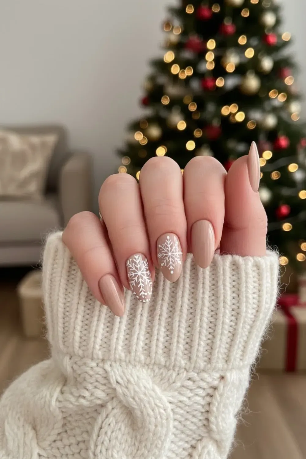 Nude Nails with White Snowflakes - Hand in a knit sweater showing beige nails with intricate hand-painted white snowflakes.