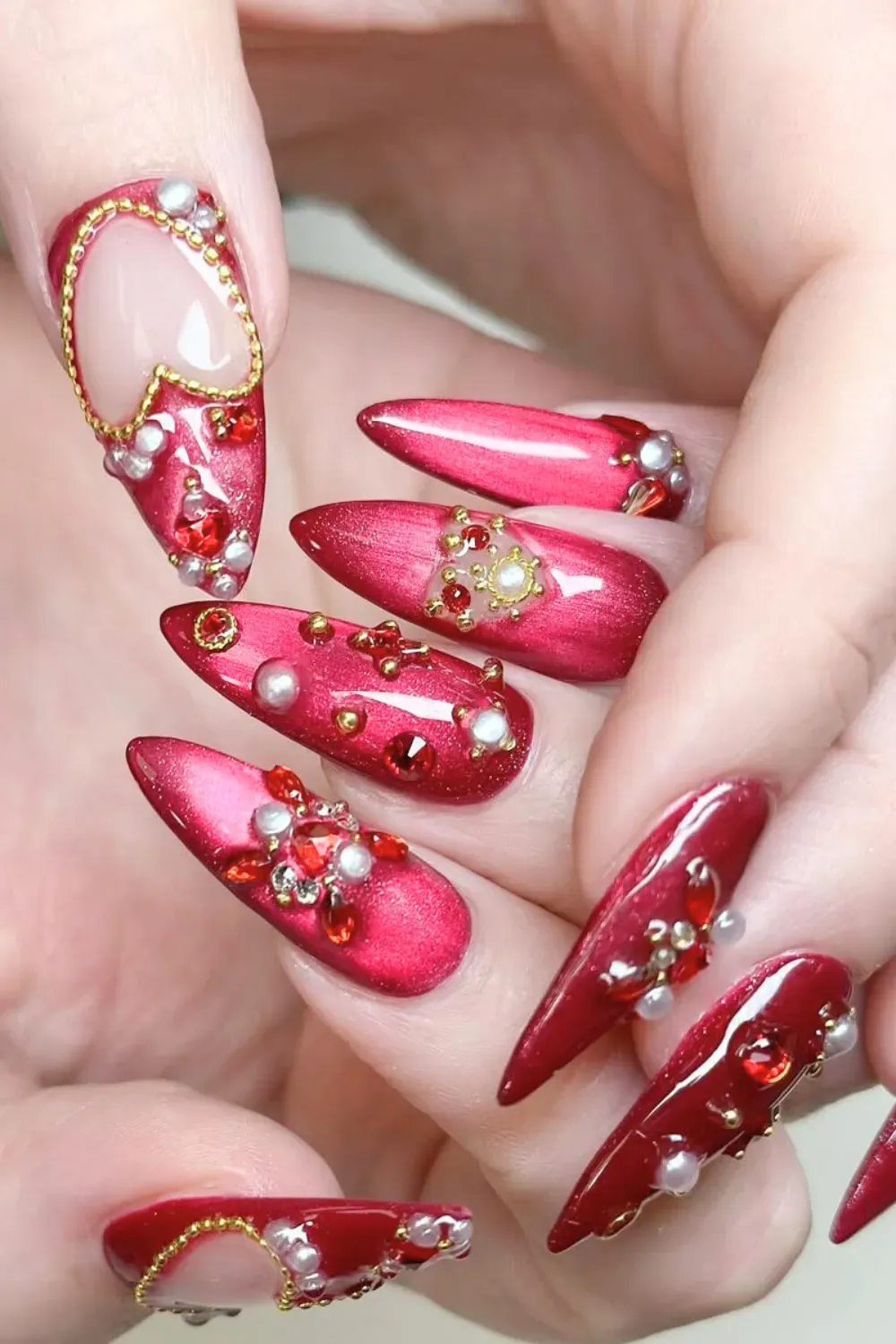 Jeweled Stiletto Red and Gold Nails - Elaborate stiletto nails with red polish, gold beads, and large ruby gemstones.