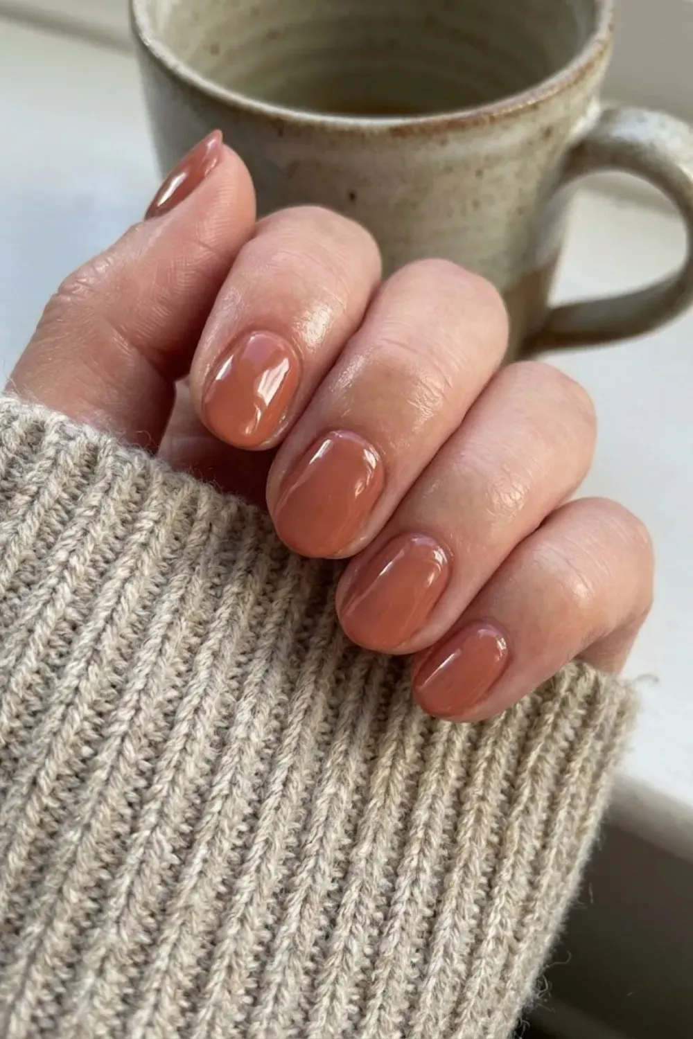 Glossy Terracotta Oval - Short oval nails in a warm, muted terracotta color with a glossy finish, giving a sophisticated earth-tone vibe.
