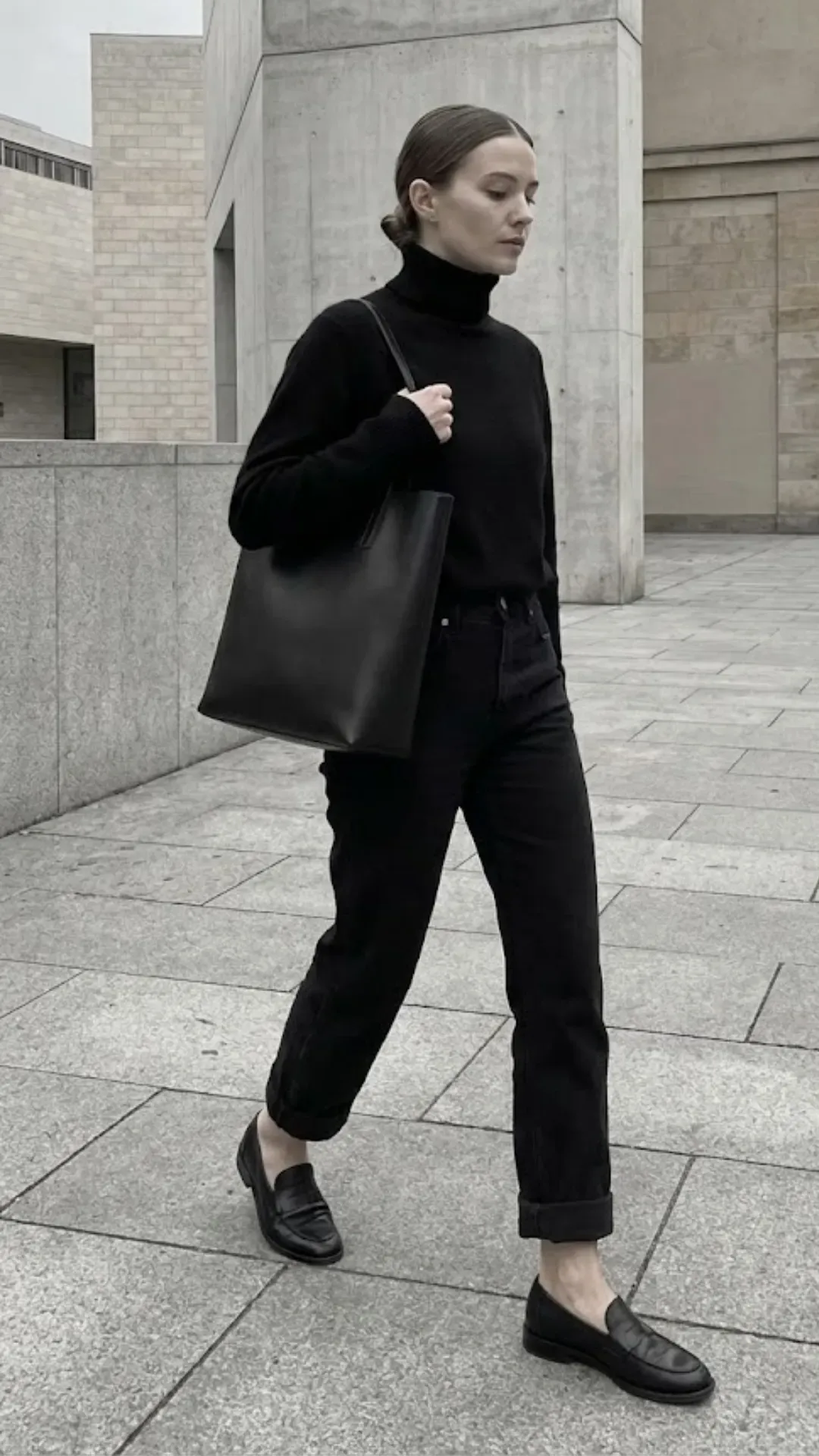 Monochrome All Black Outfit - Woman wearing an all-black outfit with black cuffed jeans, turtleneck, and loafers on a clean urban street