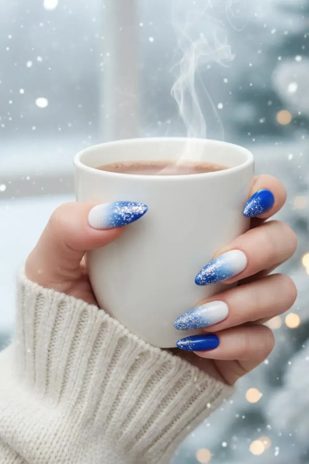 Icy Blue and White Ombré Nails - Hand holding a cup by a window, featuring a blue-to-white gradient with a dusting of frost-like glitter.