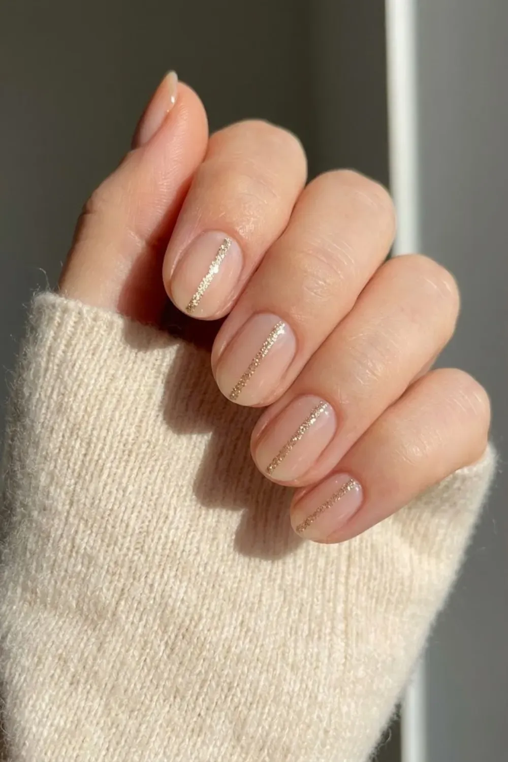 Nude with Vertical Gold Glitter Line - Minimalist nail art featuring short nude oval nails with a single fine vertical gold glitter line down the center.