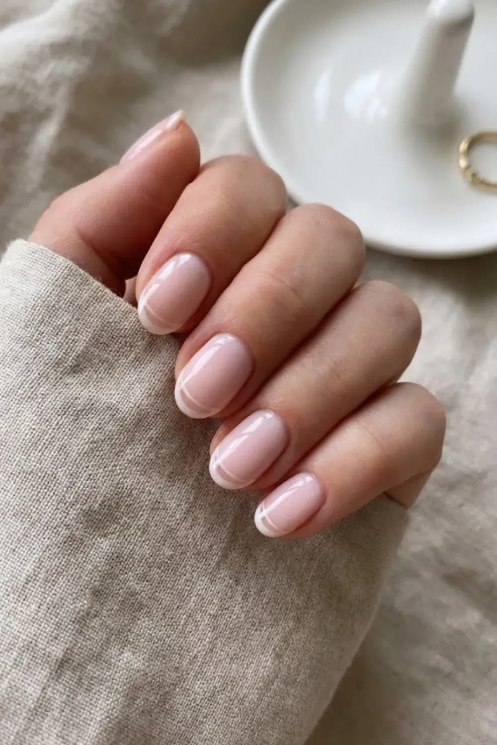 .Short Oval Milky Micro French – Close-up of short square nails with a sheer milky base and thin white micro french tips.