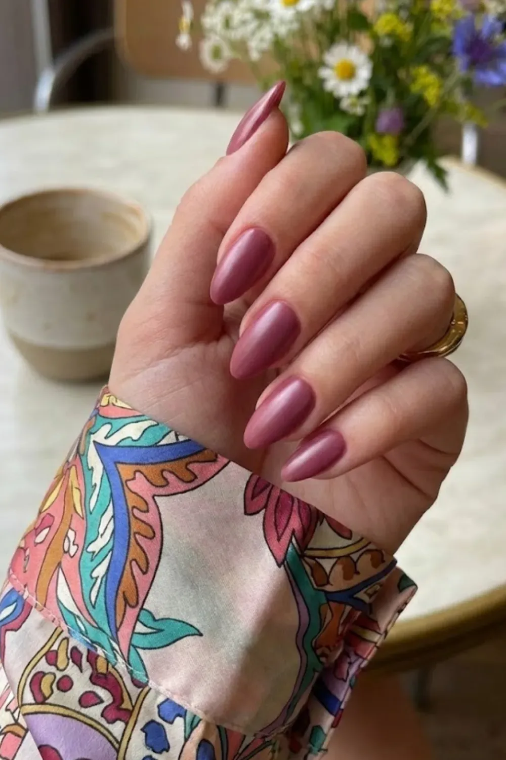 Soft Berry Pink Almond Nails – Almond-shaped nails painted in a soft berry pink shade, styled with a colorful patterned sleeve.
