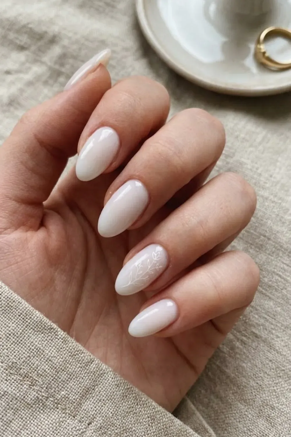 Delicate White Floral Art – Almond milky white nails with subtle minimalist white floral line art on accent nail.
