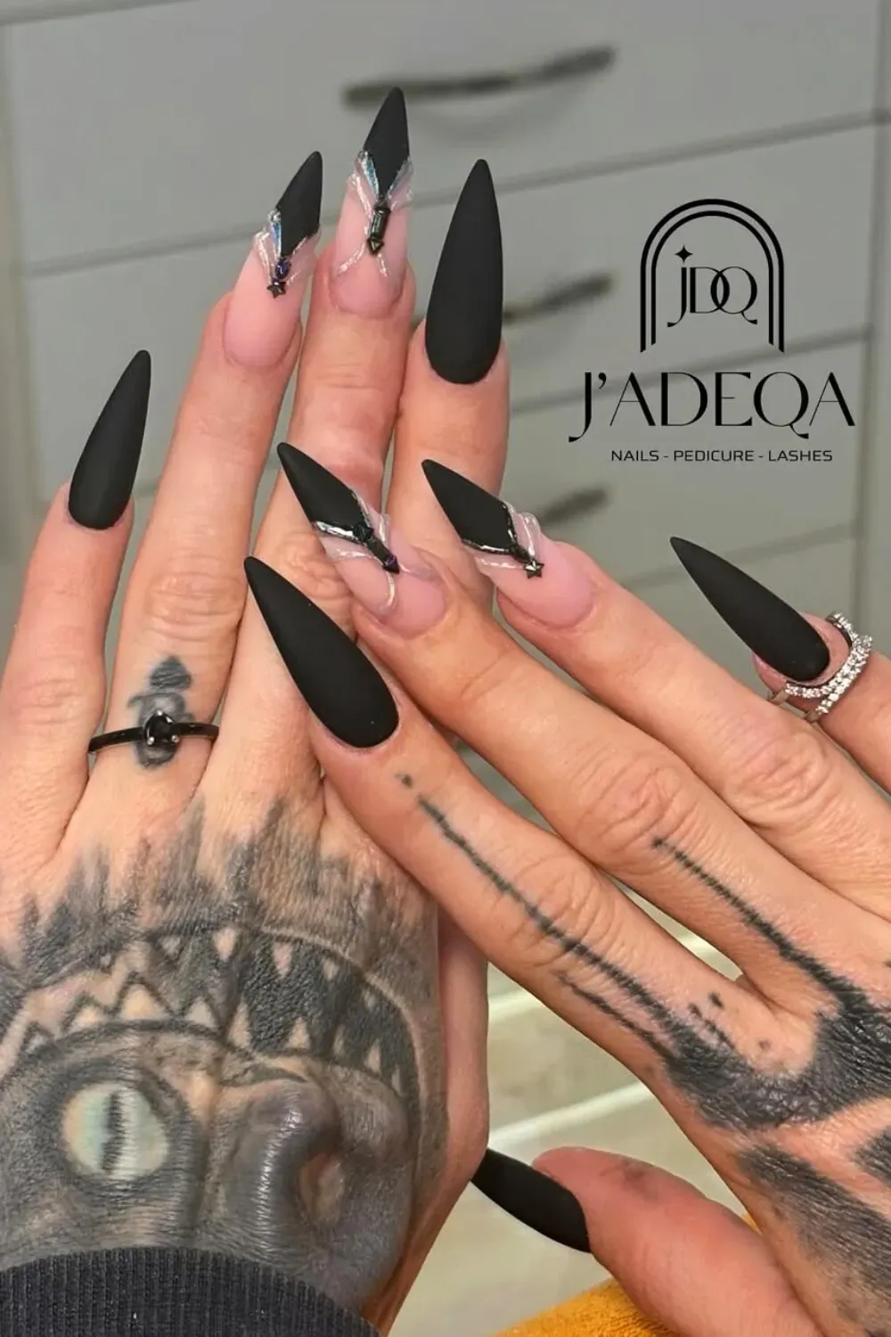 Matte Stiletto with Chrome Art	Long matte black stiletto nails with nude accent nails featuring black V-tips and iridescent chrome fine-line art and gems