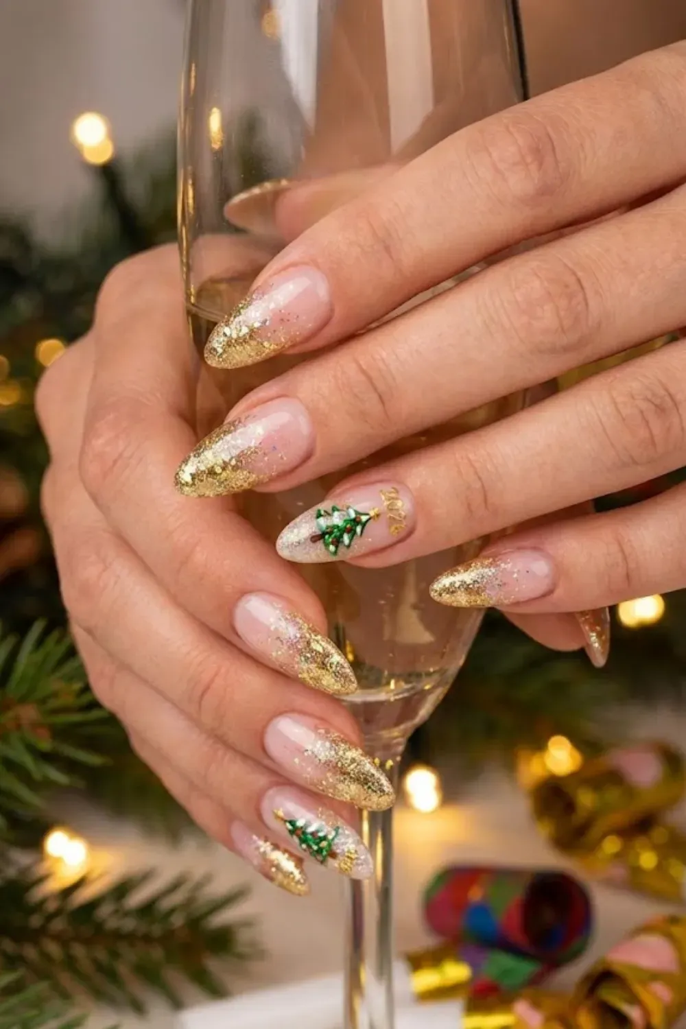 Gold Glitter Tree Nails — gold glitter French tips on almond nails with a gem Christmas tree and "2025" text