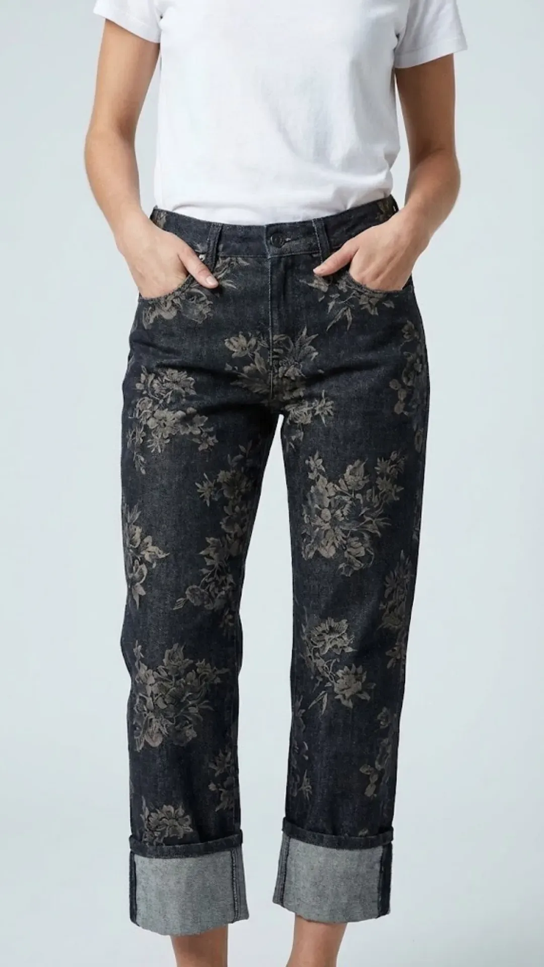 Textured Floral Cuffed Denim - Close-up detail of textured denim jeans featuring a laser-printed floral pattern and large folded cuffs with hands in pockets