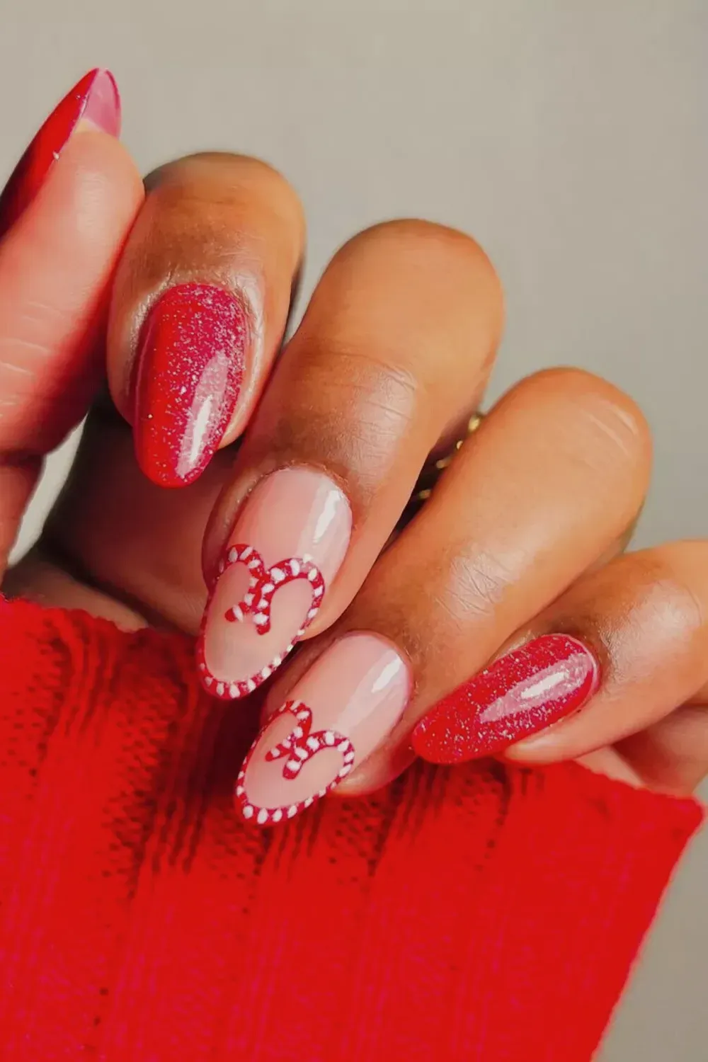 Short Red Nails with Candy Cane Hearts - Short oval nails with red glitter polish and negative space candy cane heart nail art.