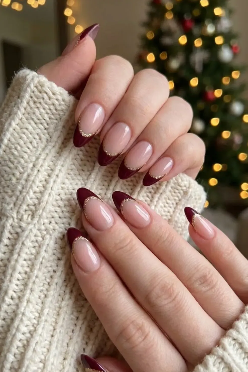 Burgundy French Tips with Gold Outline - Hand in a sweater showing deep burgundy French tips separated by a thin gold glitter line.
