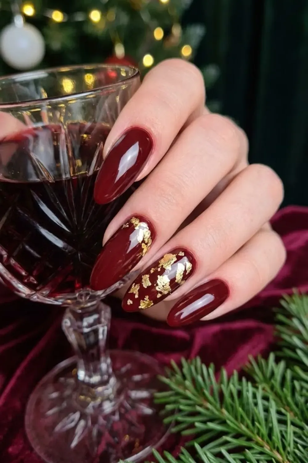 Deep Burgundy Almond Nails with Gold Foil - Dark burgundy holiday nails accented with scattered gold foil flakes for an elegant evening look.