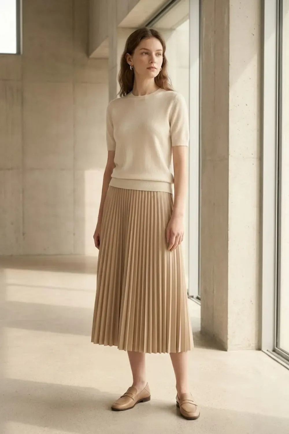Short-Sleeve Knit & Pleated Midi Skirt – Woman wearing a beige short-sleeve cashmere top and a matching beige pleated midi skirt with brown loafers, standing in a minimalist concrete space.