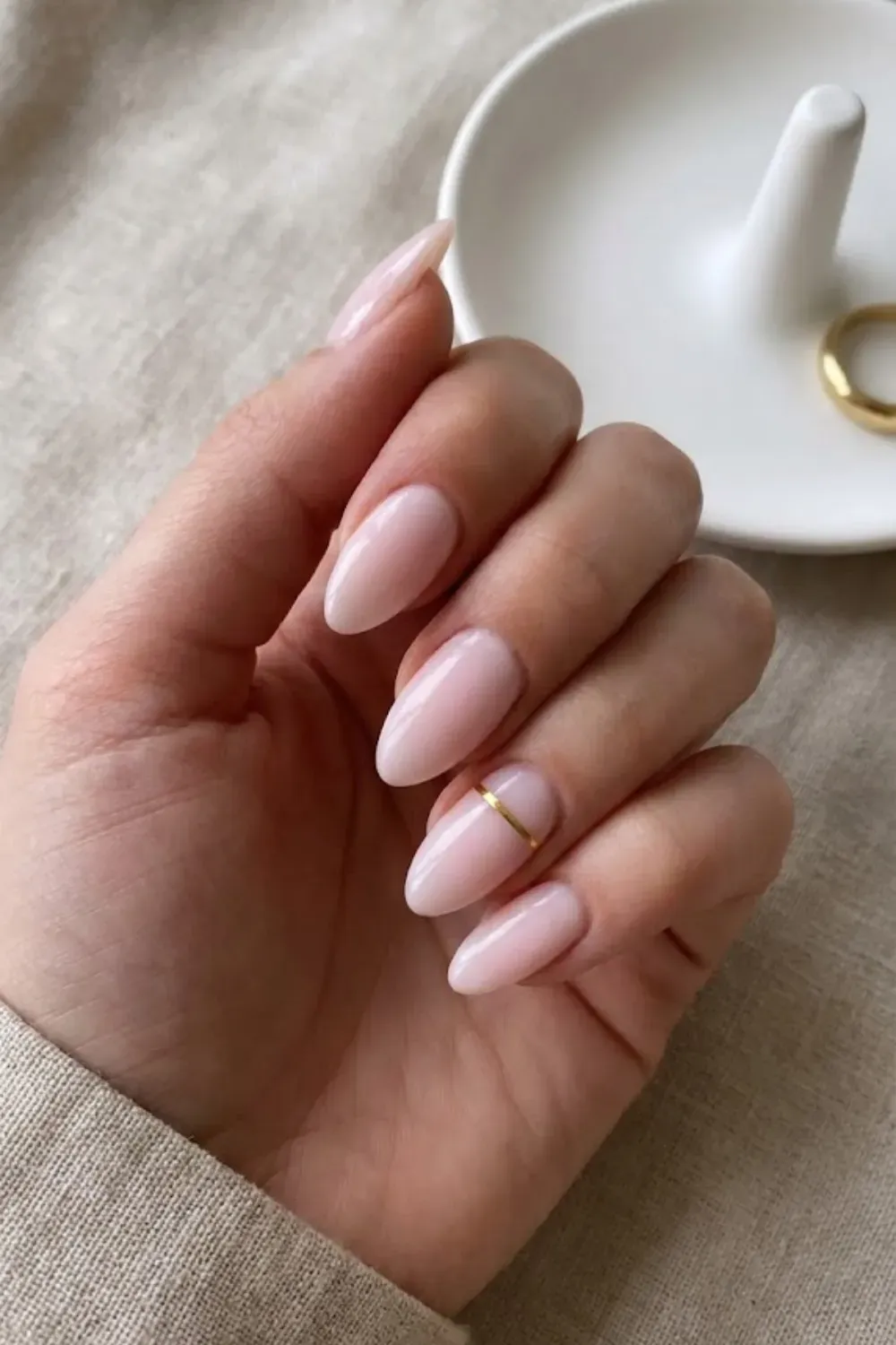 Pink with Gold Band – Almond milky pink nails featuring a metallic gold horizontal band on the ring finger.