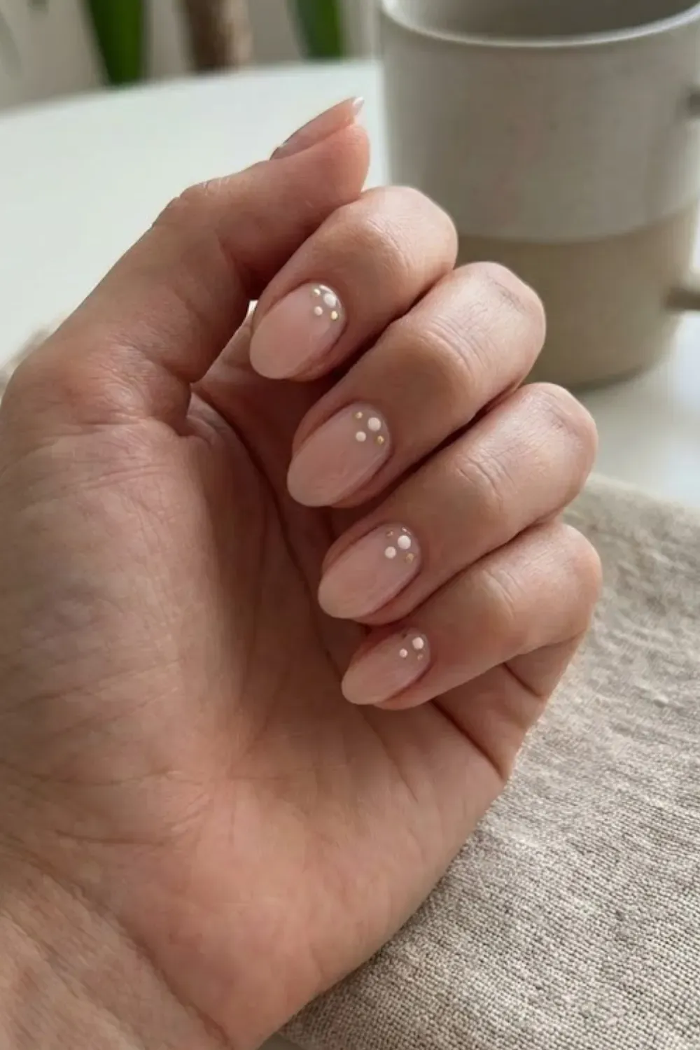 Gold and White Dot Cluster – Oval sheer pink nails decorated with a tiny cluster of white and gold dots at the base.