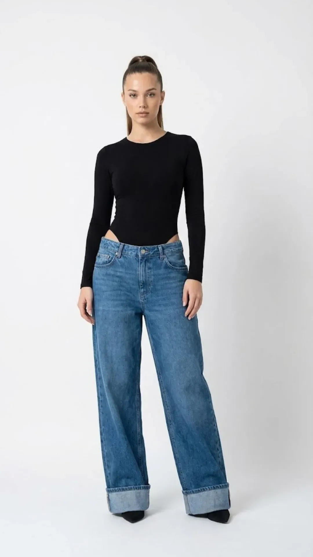 Wide Leg Jeans and Bodysuit - Fashion shot of a woman wearing voluminous wide-leg cuffed blue jeans with a fitted black bodysuit against a white background