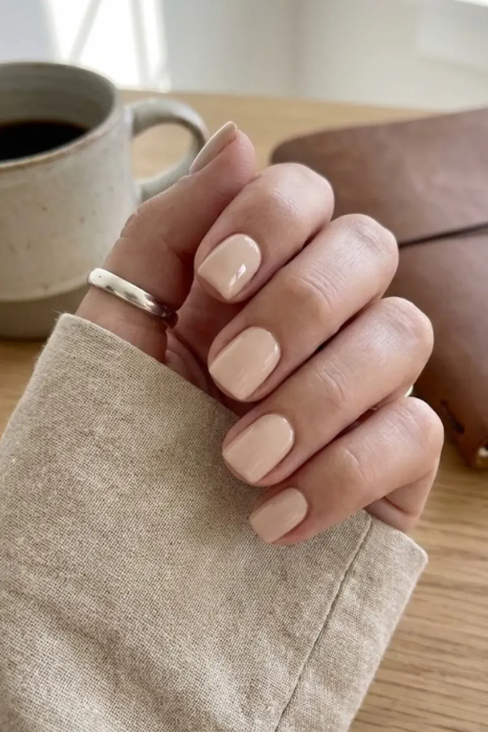 Creamy Nude Short Square Nails – Short square nails with a glossy creamy nude polish, styled with a silver ring and coffee cup.
