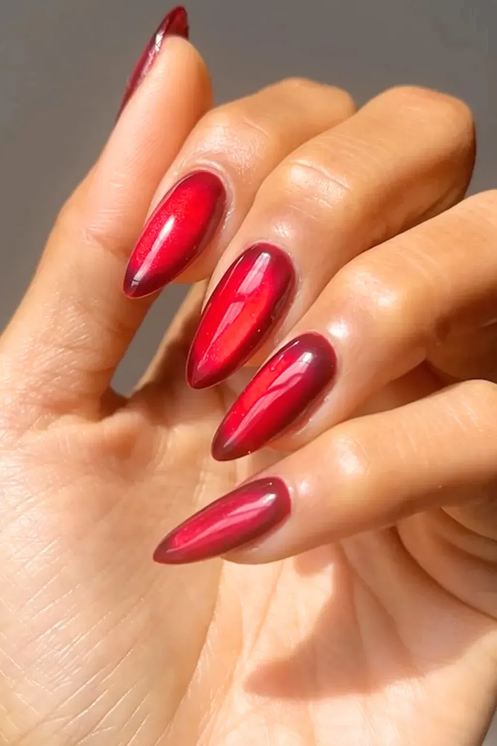 Metallic Red Chrome Almond Nails - High-shine metallic ruby red chrome nails in a sharp almond shape.