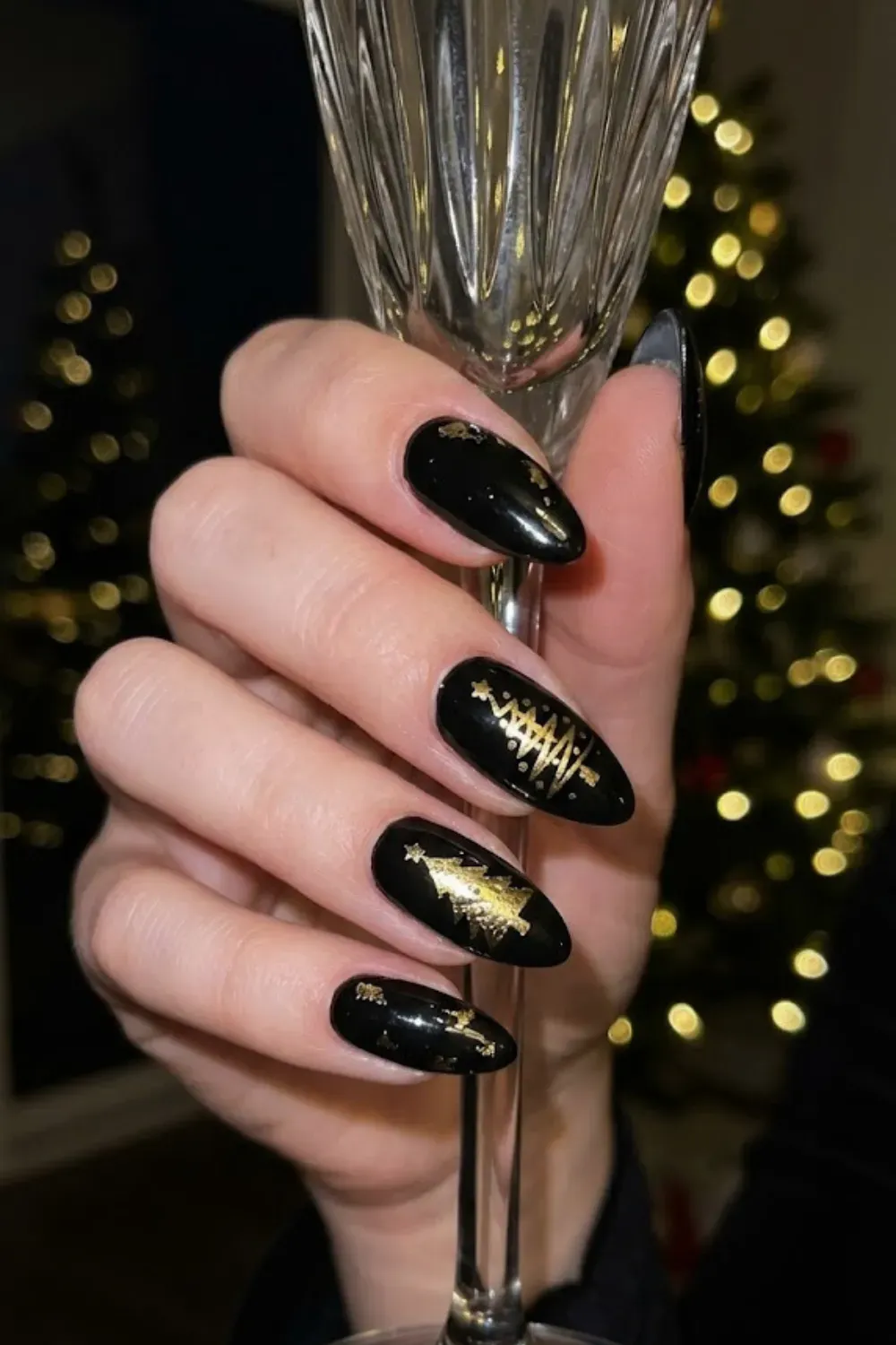 Black Almond Nails with Gold Foil Christmas Trees - Glossy black almond nails decorated with abstract gold foil Christmas tree designs, offering a chic and sophisticated festive look.