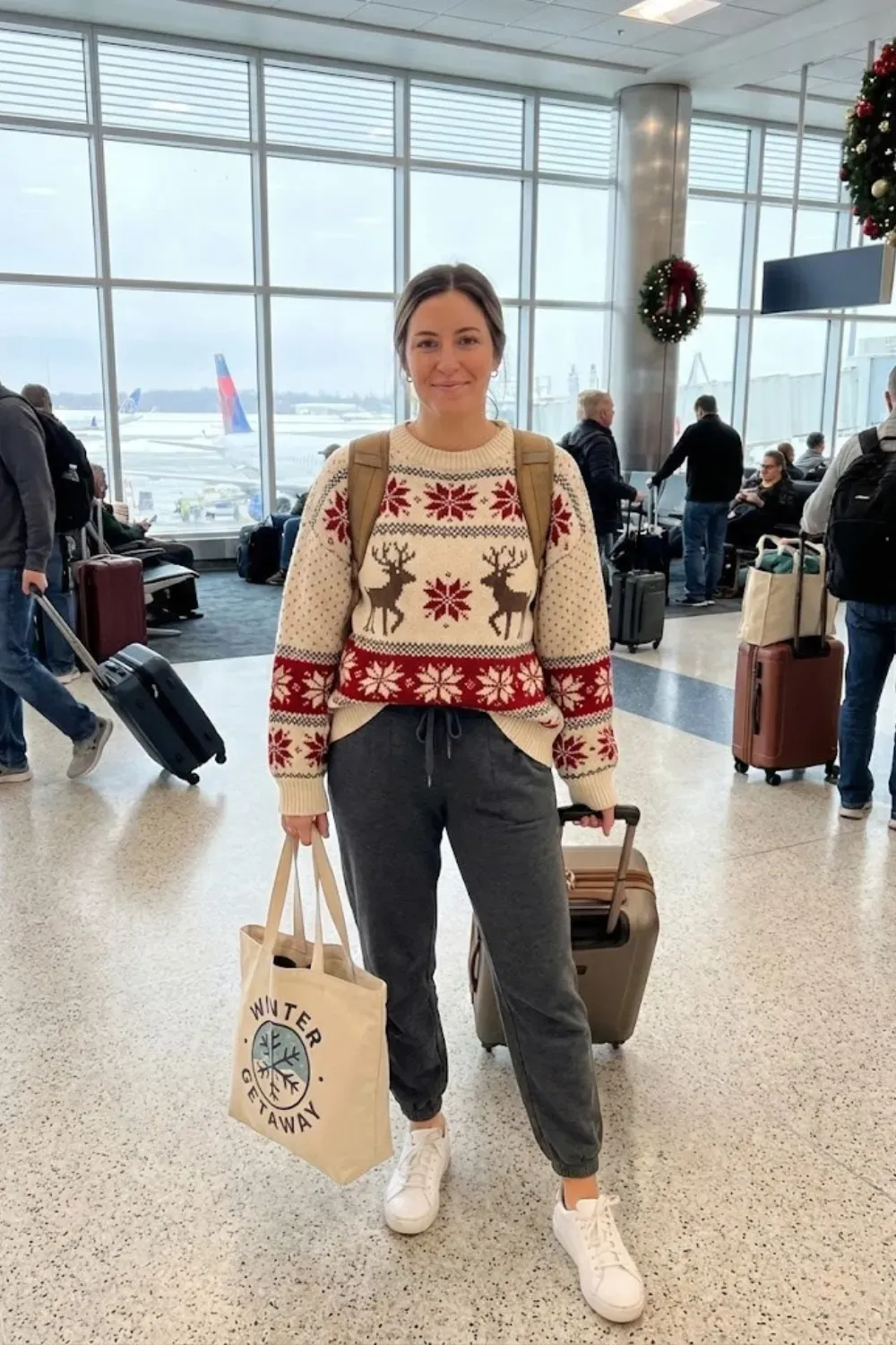 Woman at airport wearing oversized reindeer fair isle sweater and dark grey joggers for holiday travel outfit