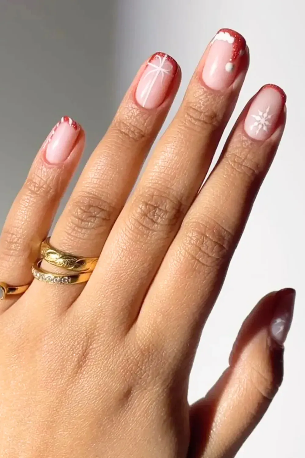 Short Nude Nails with Red Tips and Snowflakes - Natural short nails with delicate white snowflakes and thin red french tips.