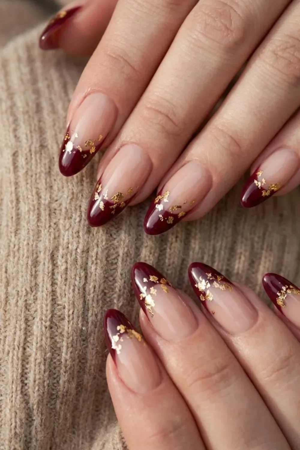 Burgundy Gold Flake Nails — long almond nails with burgundy tips and scattered gold foil flakes.