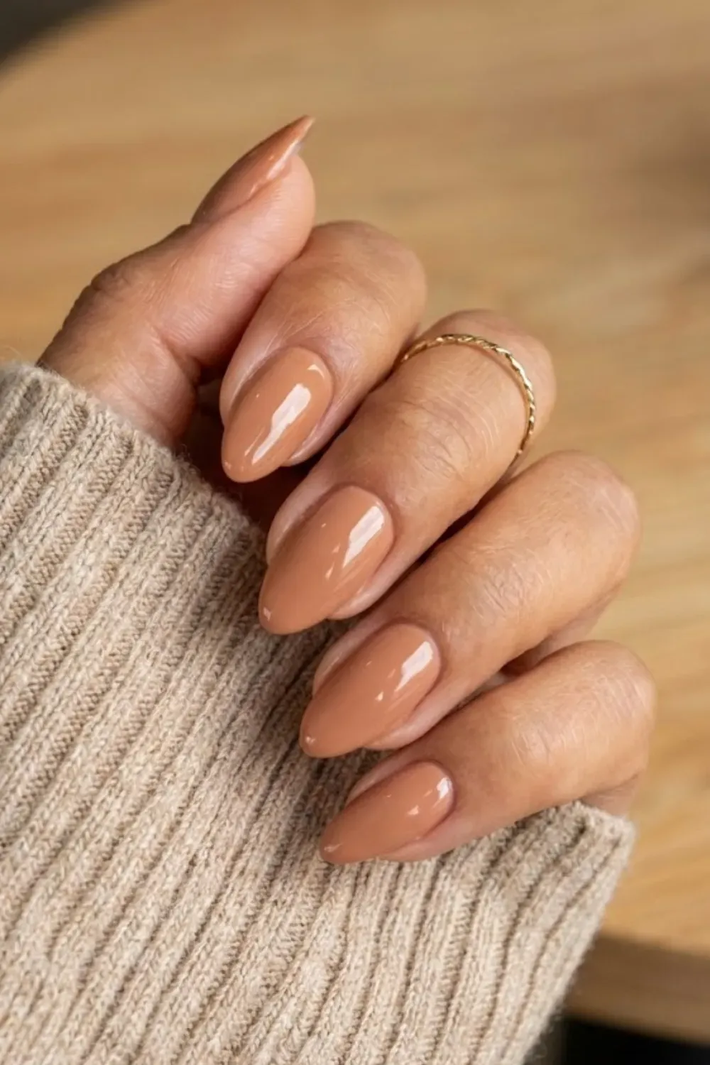 Glossy Caramel Almond Nails – Almond-shaped nails painted in a warm glossy caramel brown shade, paired with a beige knit sweater.