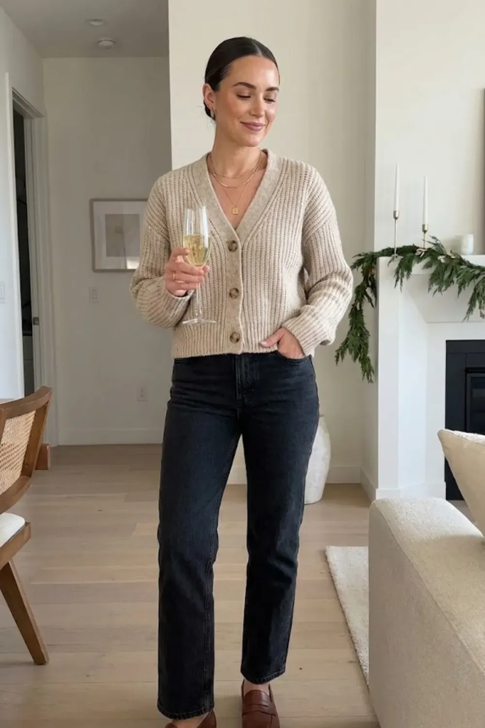 Cozy Cardigan & Dark Denim – Woman in beige chunky buttoned cardigan and black straight-leg jeans holding a glass of champagne.