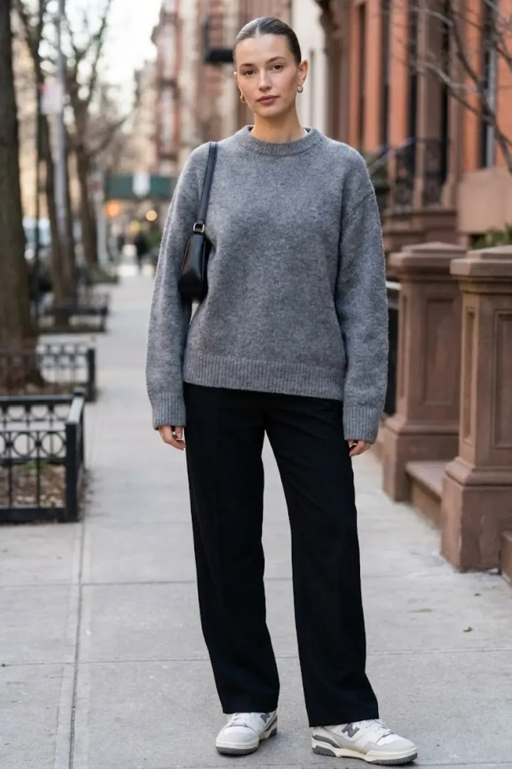 Woman on city street wearing relaxed grey wool crewneck and black trousers urban winter look.