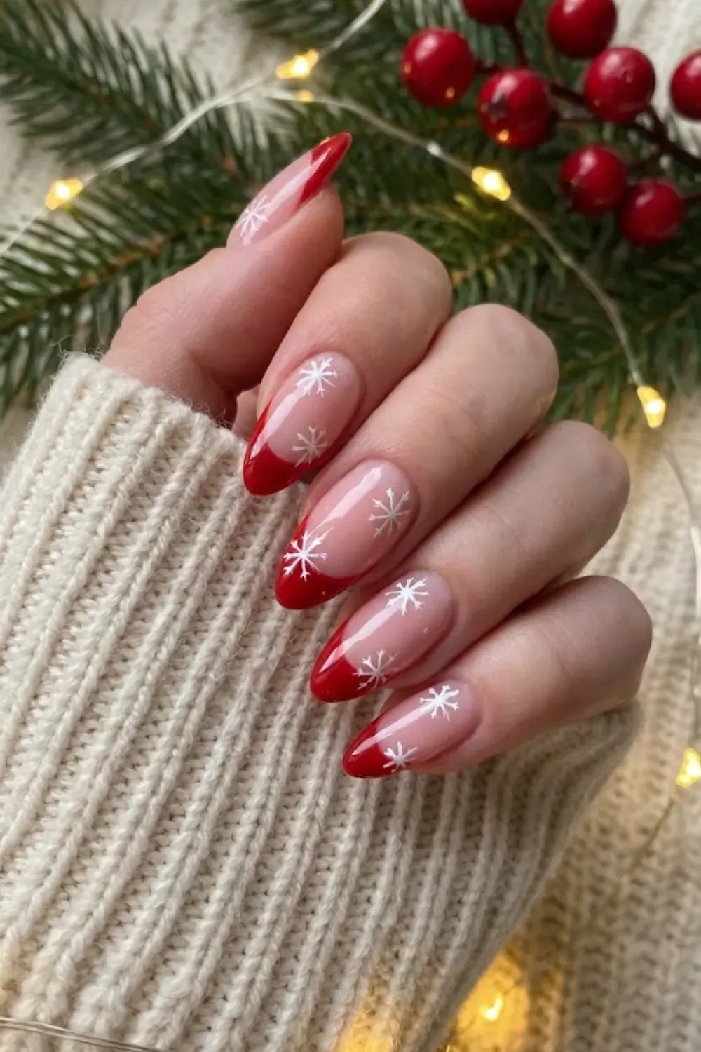 Red French Tip Almond Nails with Snowflakes - Nude almond nails featuring bright red French tips and dainty white snowflake nail art.
