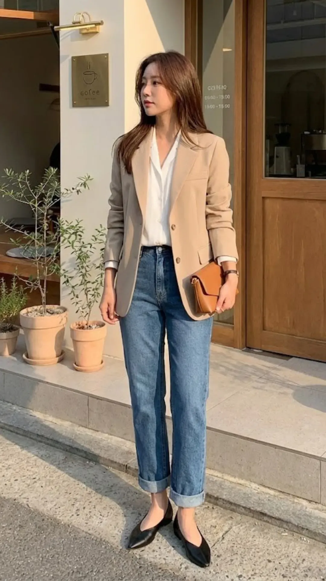 Office Casual Cuffed Denim - Woman wearing cuffed straight-leg jeans with a beige blazer and pointed flats standing near a cafe