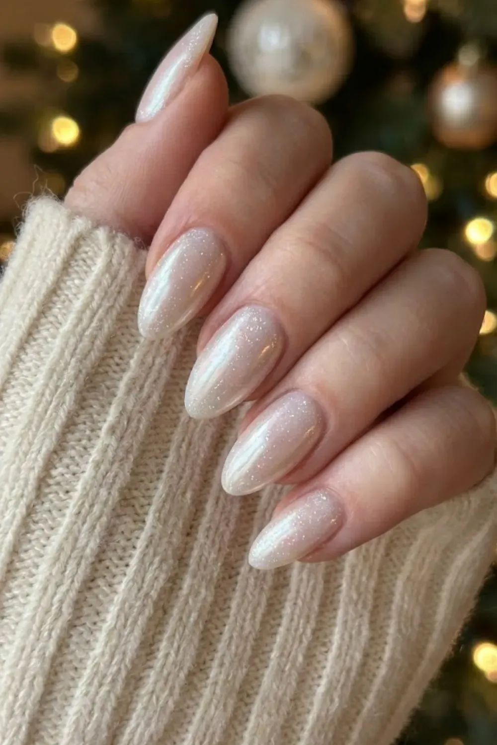 Pearlescent White Chrome Nails - Hand in a cream sweater featuring almond nails with a shimmering, milky white pearl chrome finish.