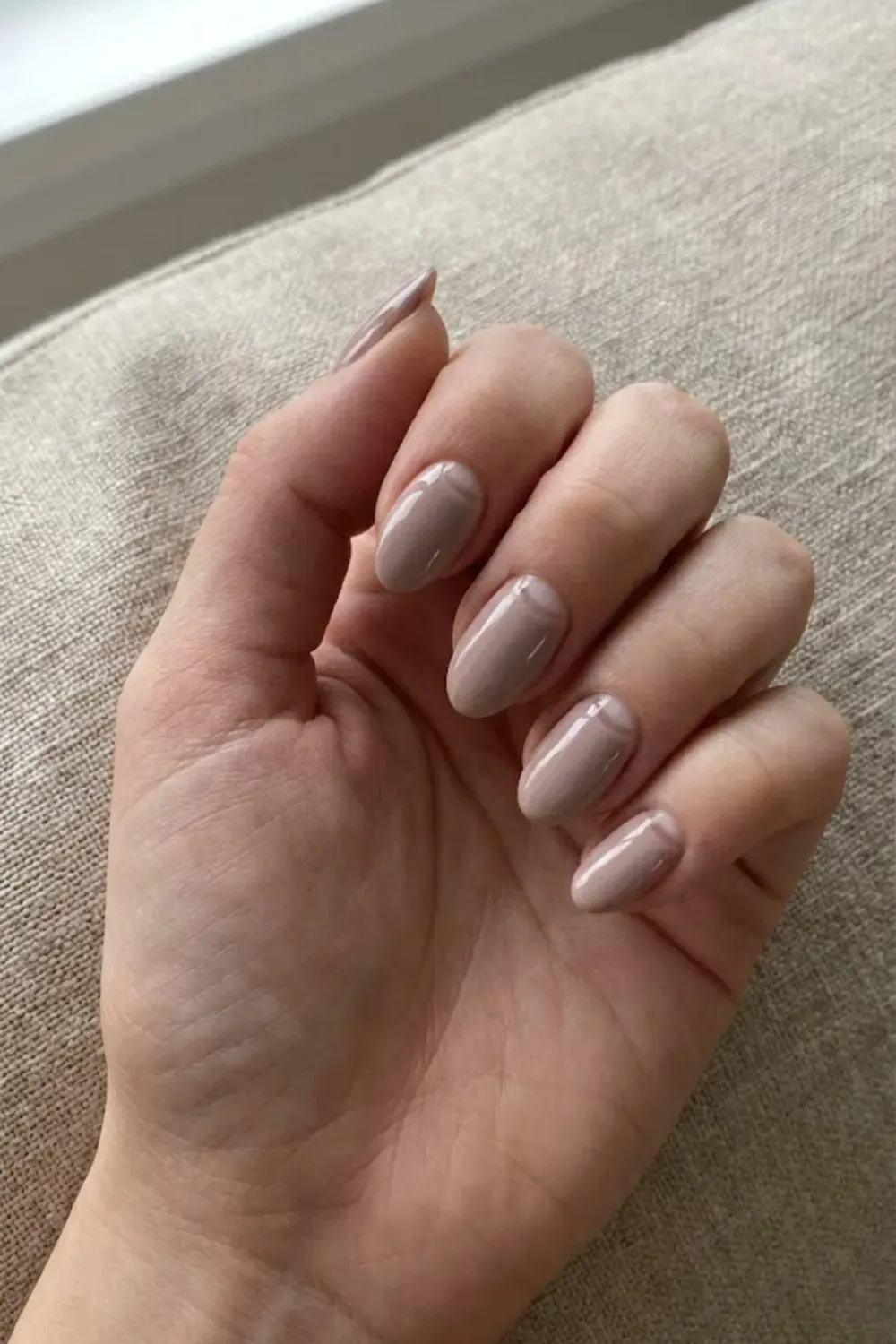 Taupe Negative Space Half-Moon – Glossy taupe oval nails with a negative space half-moon design at the cuticle.
