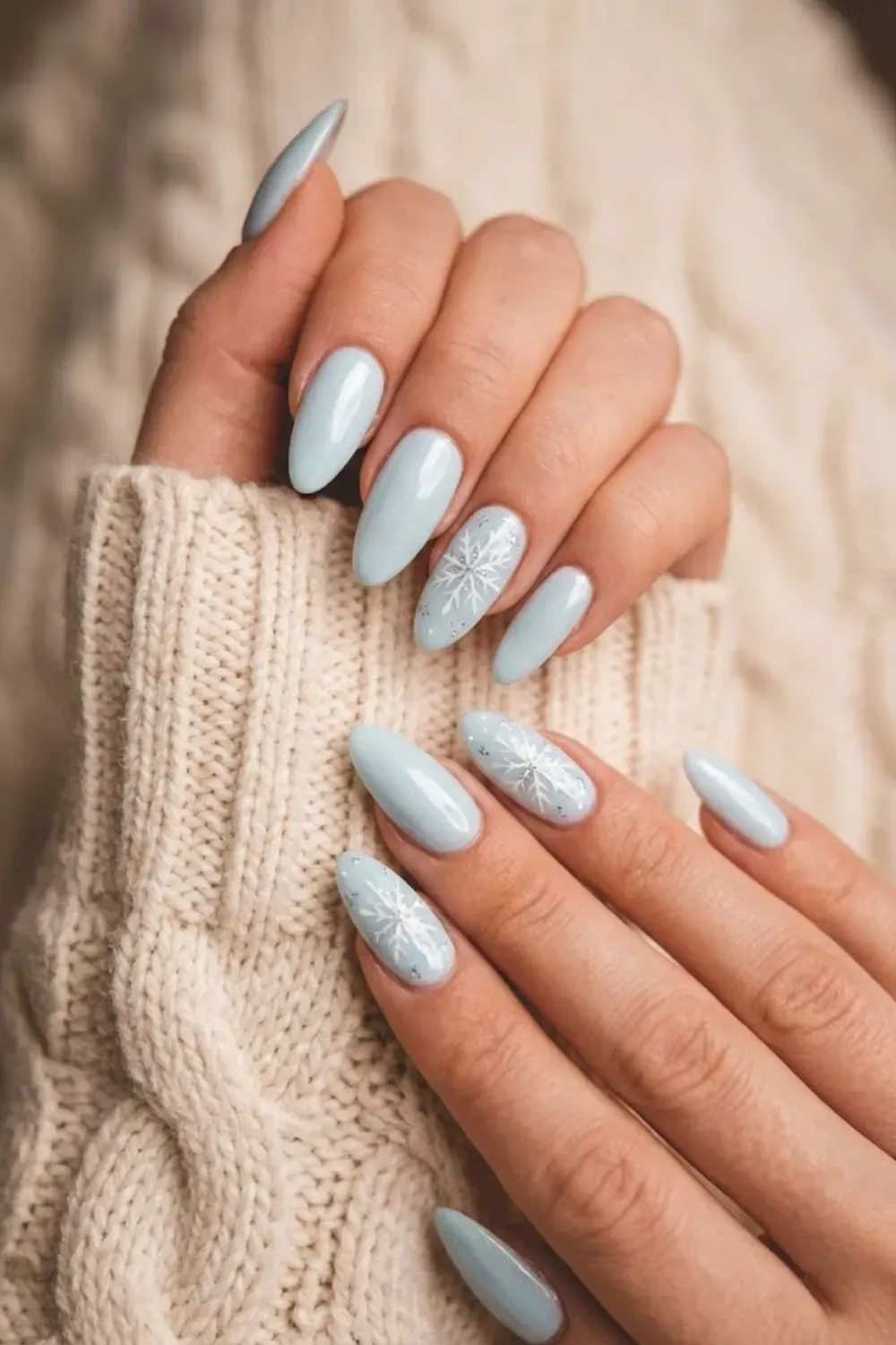Soft Blue Almond Nails with White Snowflakes – Light icy blue almond nails featuring hand-painted white snowflakes and subtle silver glitter accents, perfect for winter nail trends.