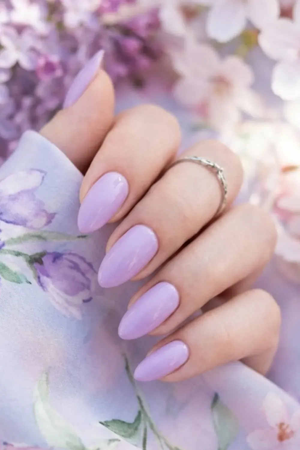 Almond shaped nails in a vibrant but soft lilac purple, surrounded by spring flowers.