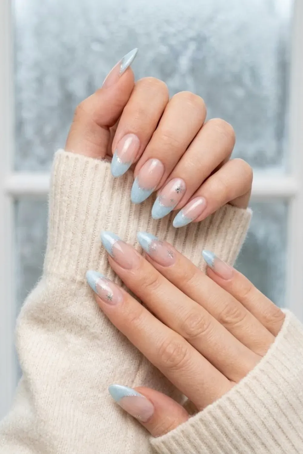 Icy Blue Glitter French Tip Almond Nails – Almond-shaped nails with sparkling icy blue glitter French tips and snowflake accents on a nude base, a minimal winter look.