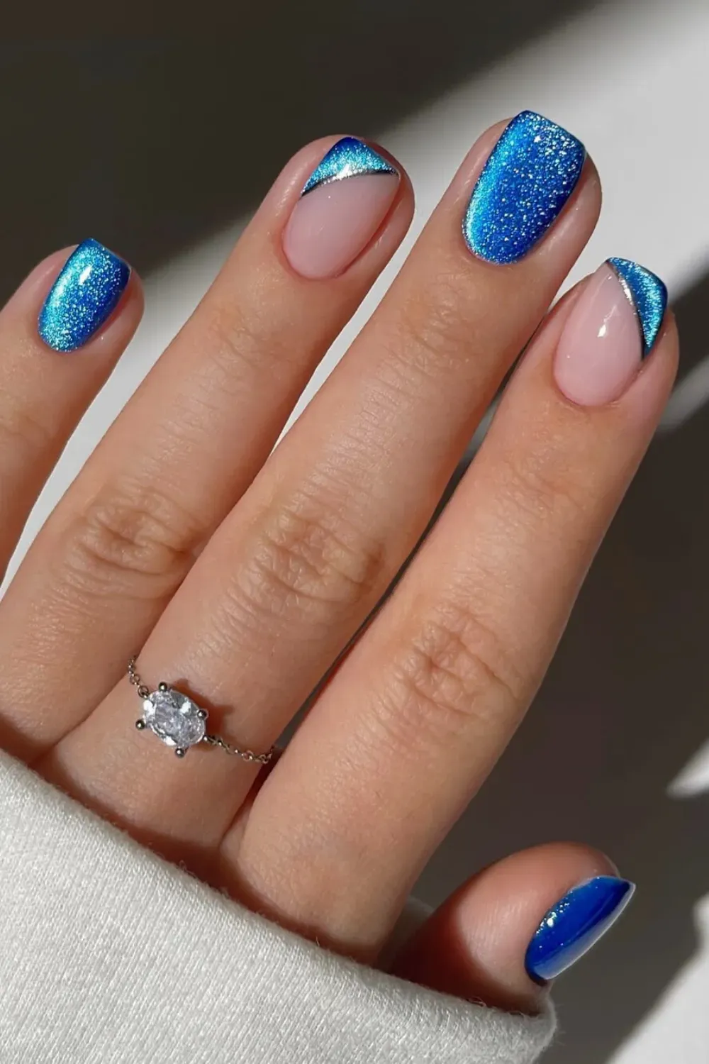 Glitter Blue and Silver Chrome Asymmetrical Tips – Short square nails with blue glitter abstract tips lined with metallic silver chrome on a clean nude base.