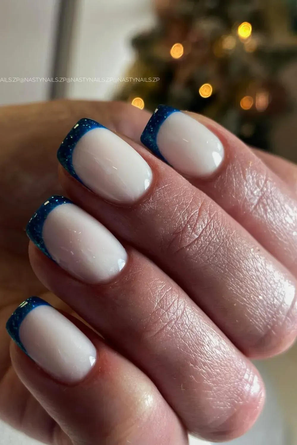 Blue Glitter Micro French Tips – Short square nails with a milky white base featuring delicate dark blue glitter French tips.