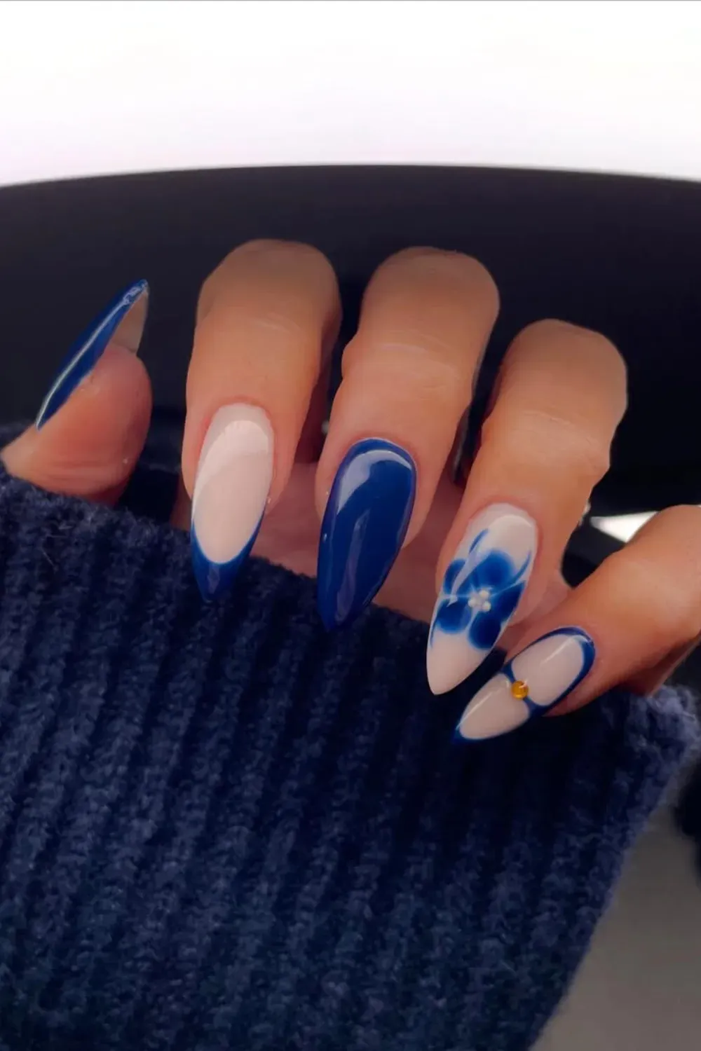 Navy French Tips with Watercolor Flower – Almond nails combining classic navy blue French tips with a statement blue watercolor floral design on the accent nail.
