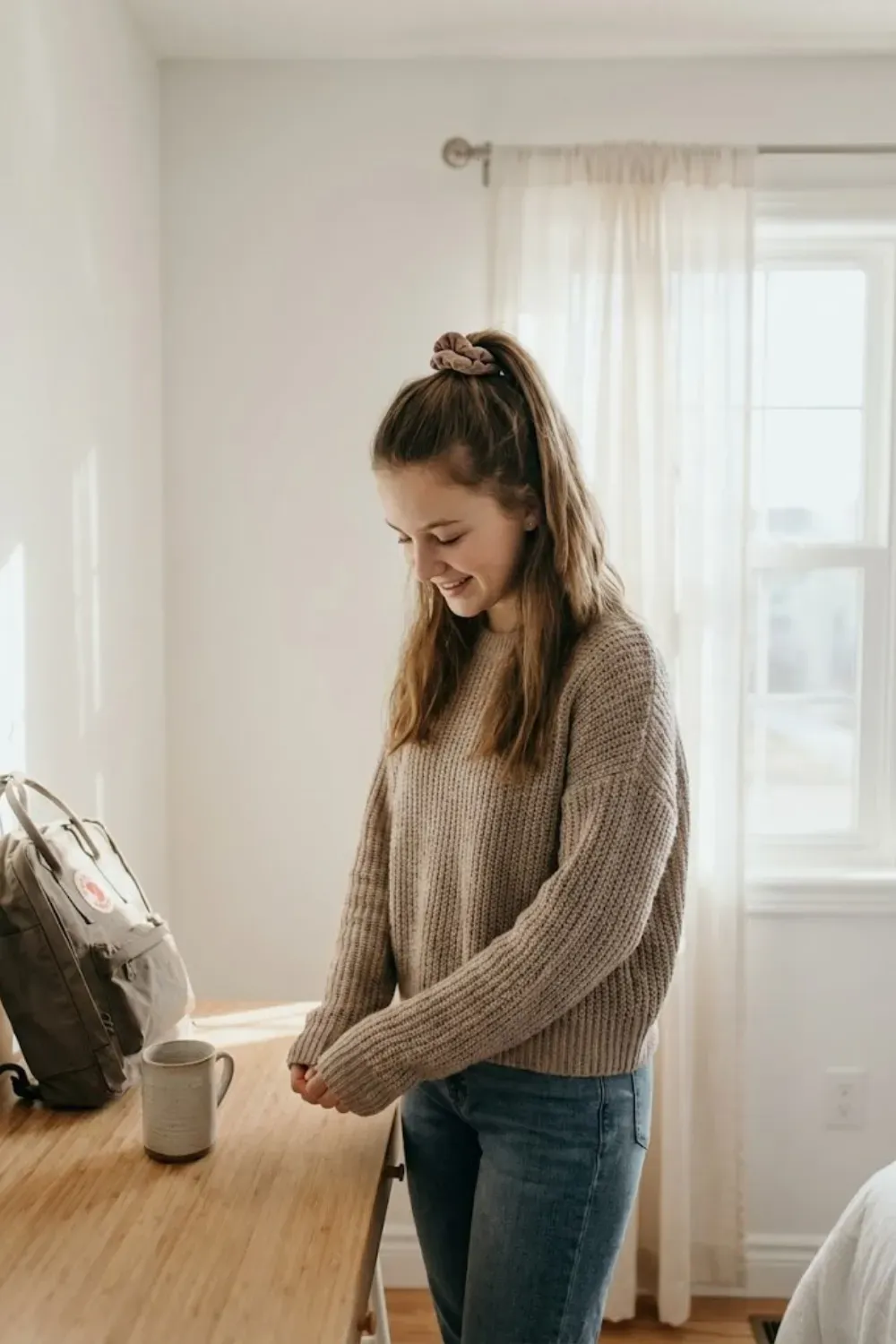 Half-Up High Ponytail with Scrunchie - Girl standing by a desk with a half-up high ponytail secured with a brown scrunchie.