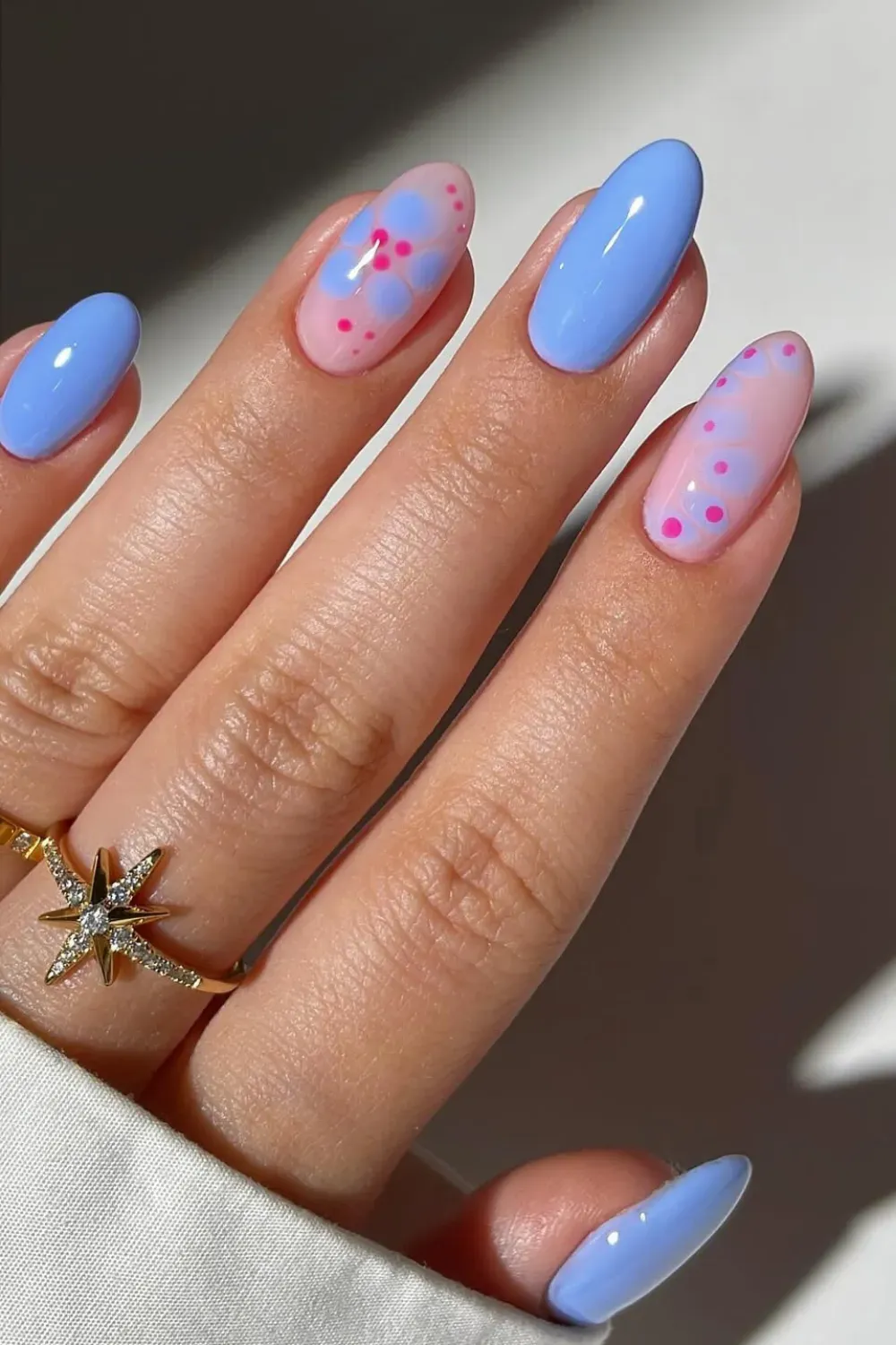 Baby Blue Blooming Gel Flowers – Soft almond nails mixing solid periwinkle blue with aura-style blooming gel flowers in blue and pink on a nude base.