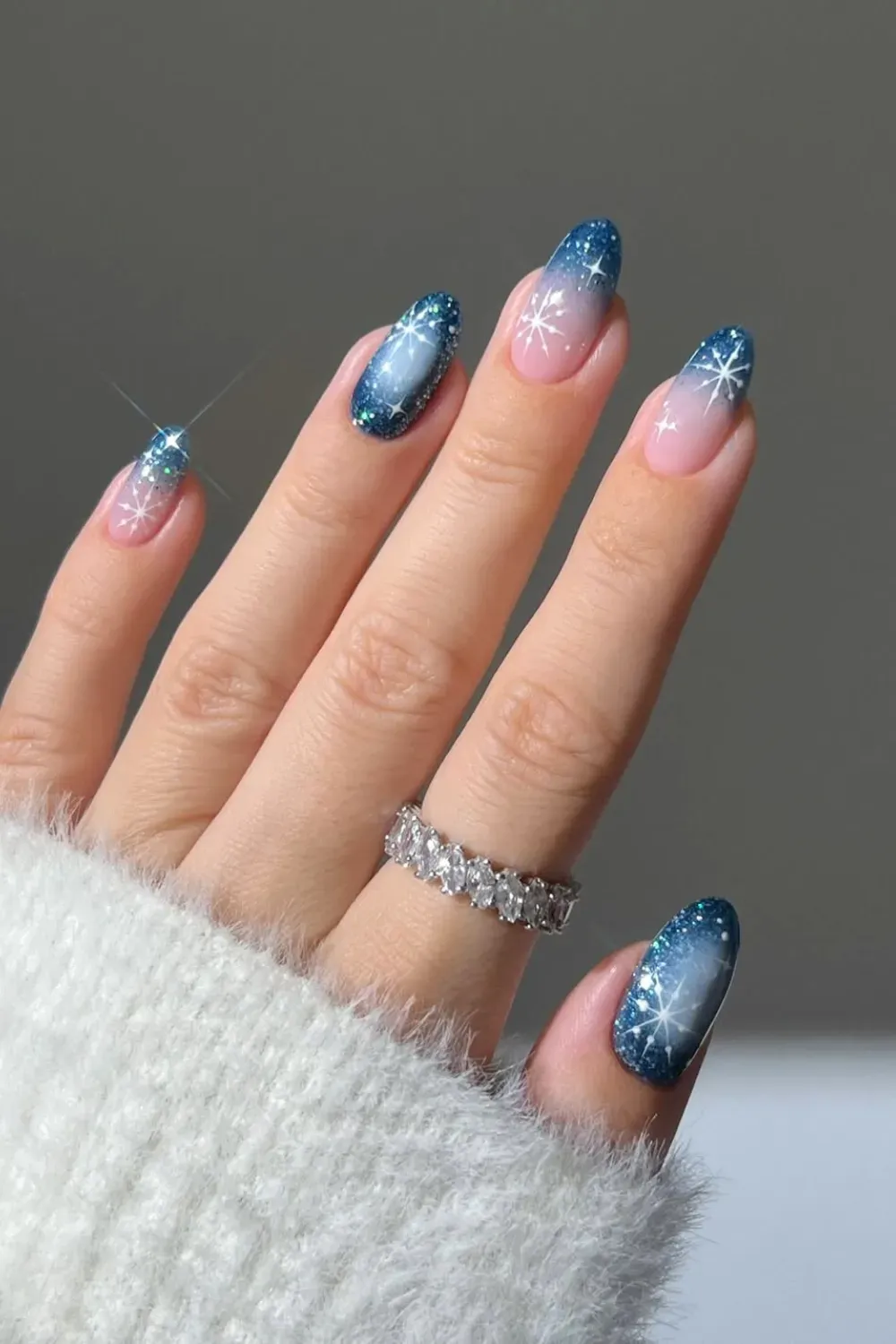 Winter Ombre Snowflake Nails – Almond nails with a nude-to-blue glitter gradient ombre, finished with delicate white hand-painted snowflakes.