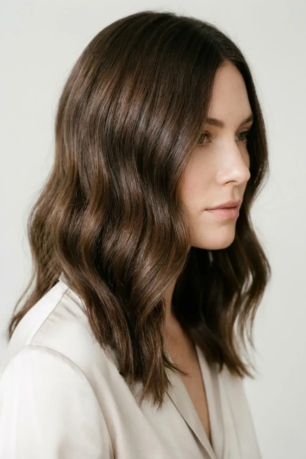Glossy Neutral Chocolate Brown – Woman with medium-length, glossy neutral chocolate brown wavy hair wearing a white silk shirt