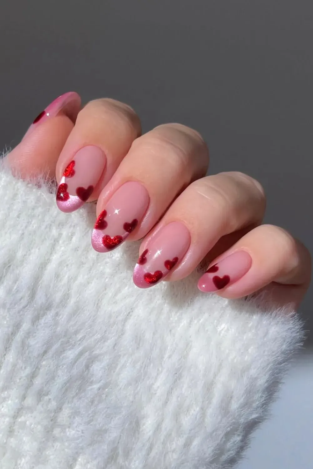 Glitter Red Heart Tip French Manicure – Oval nails with a sheer base and sparkling red glitter heart-shaped french tips.