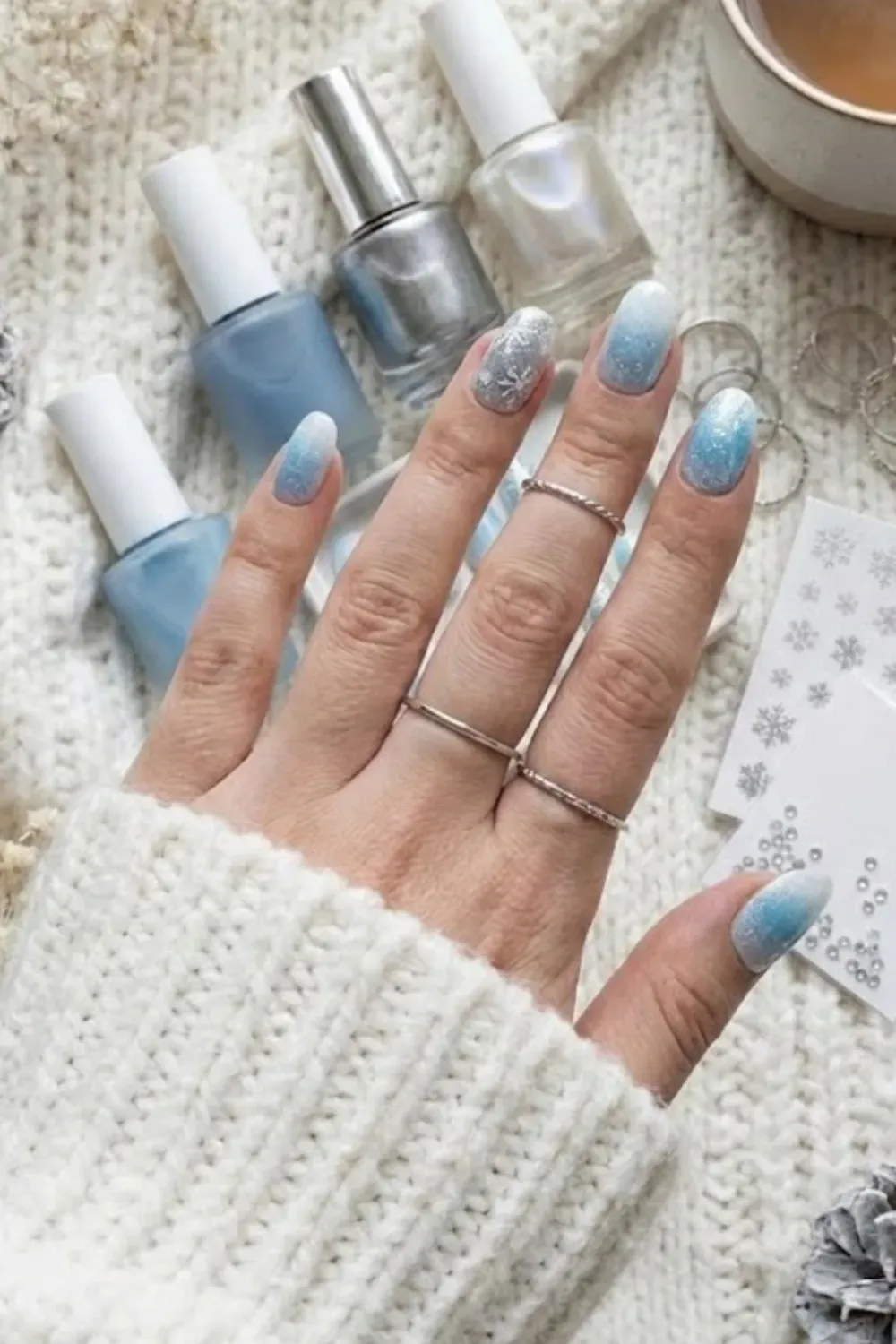 Glittery Icy Blue Winter Nail Art Flatlay – A flatlay showing glittery icy blue and white ombre nails with snowflake decals, surrounded by winter decor.