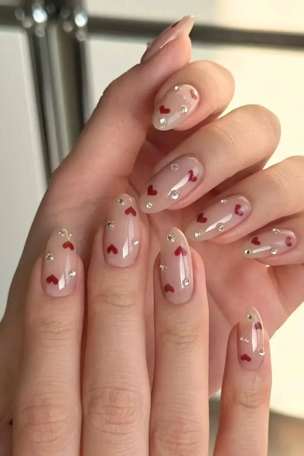 Nude Almond Nails with Rhinestones and Hearts – Sheer nude almond nails embellished with small red hearts and sparkling crystals