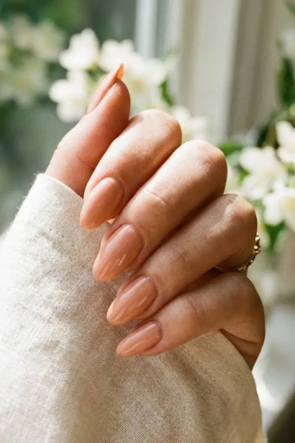 Almond nails in a warm peach nude shade, glowing in natural sunlight.