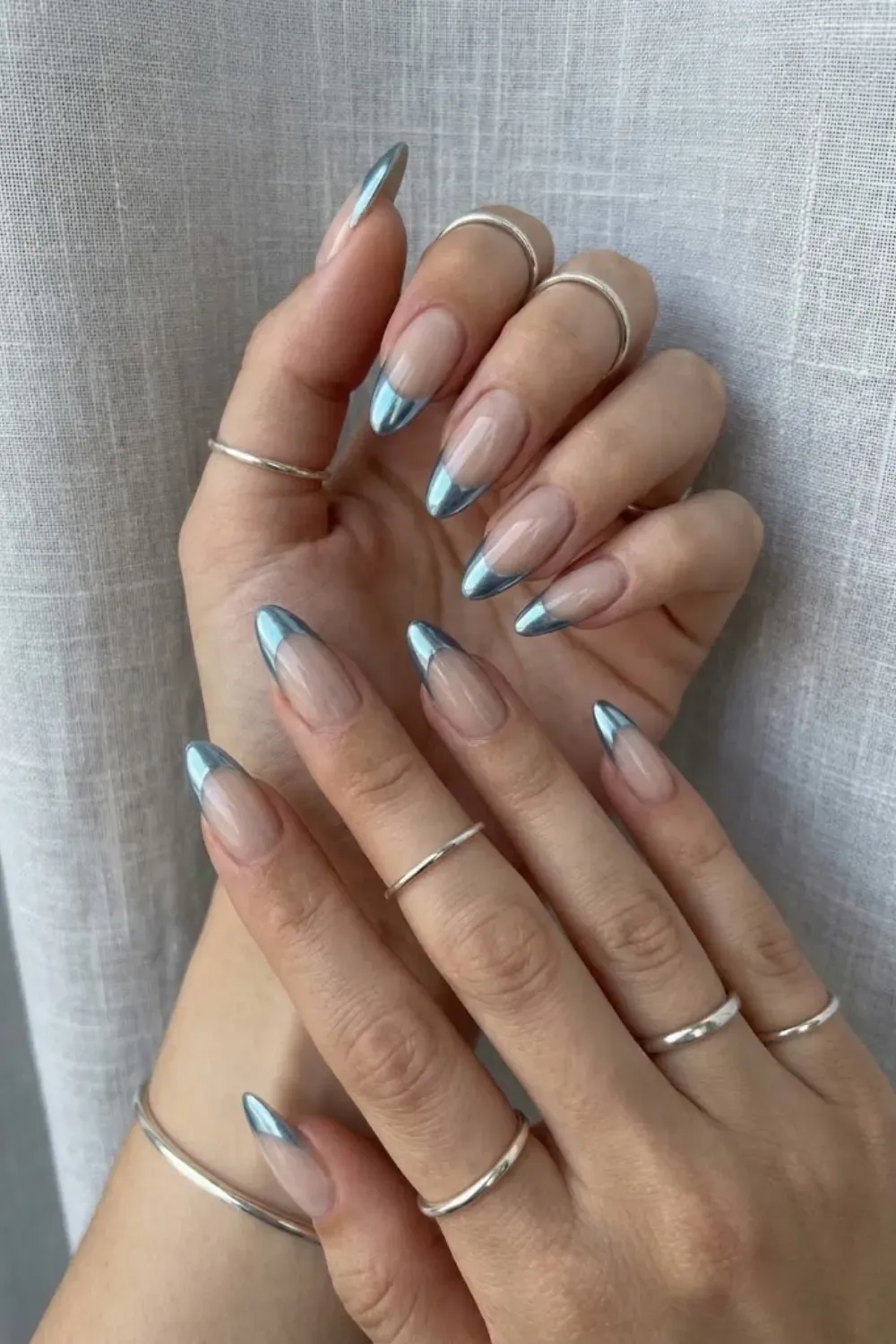 Metallic Blue Chrome French Tip Nails – Minimalist almond nails featuring metallic icy blue chrome French tips on a sheer nude base, trending for winter.