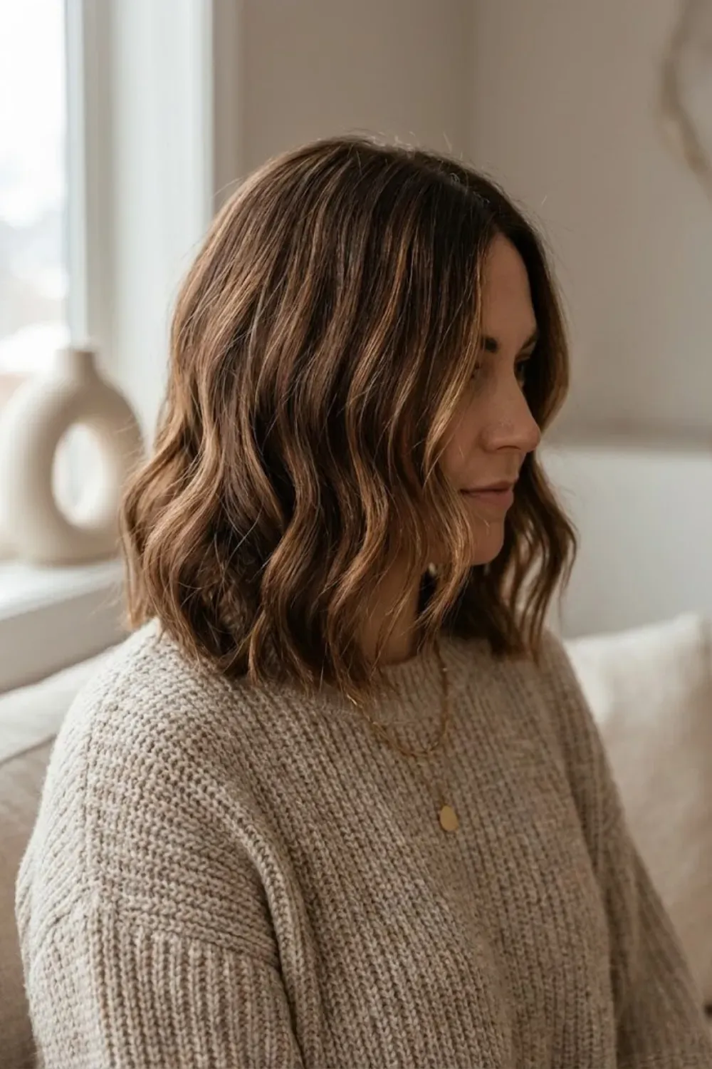 Warm Caramel Brown Balayage Lob – Woman with a textured long bob (lob) featuring warm caramel brown balayage highlights, wearing an oatmeal knit sweater