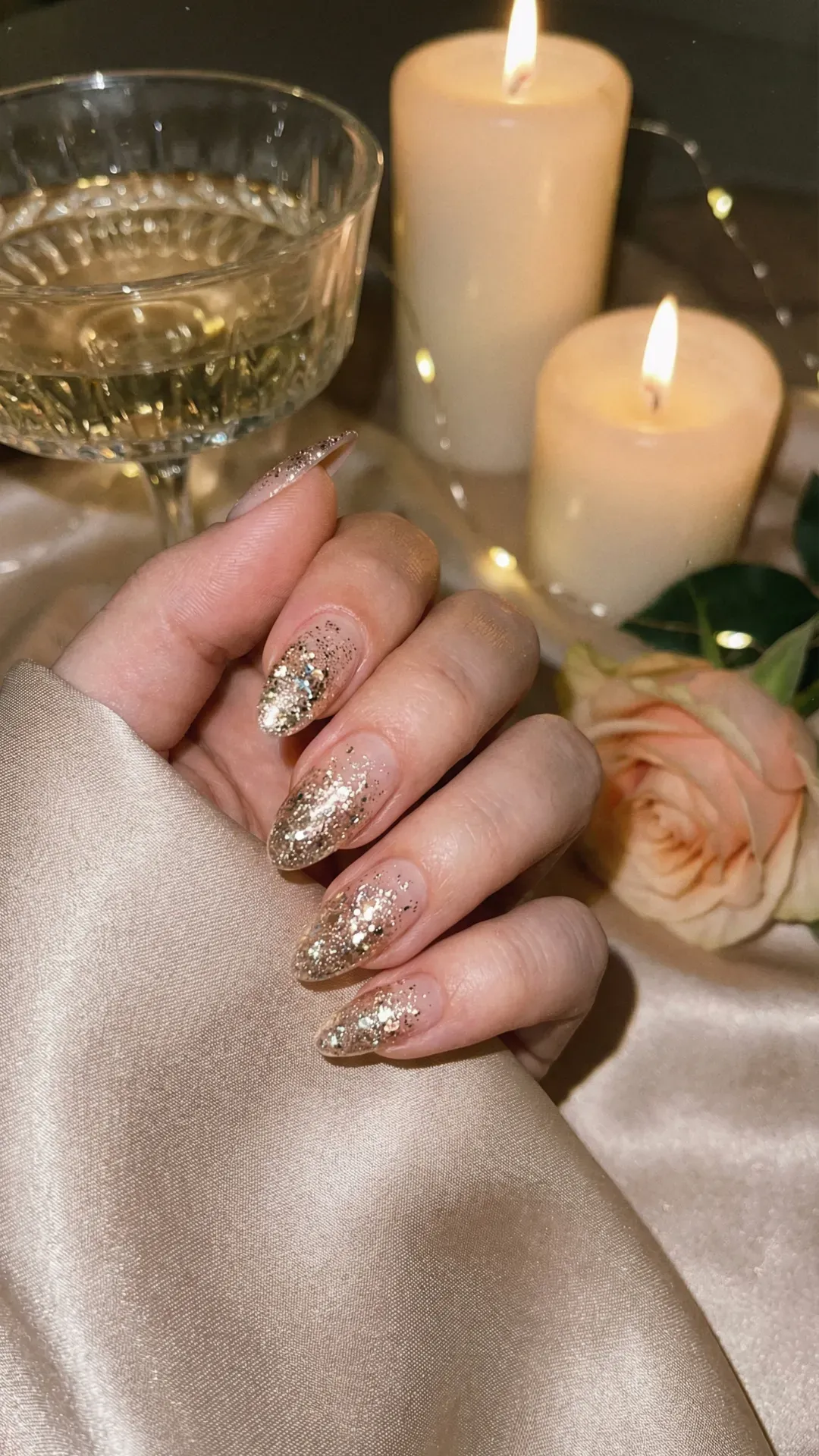 Almond-shaped nude nails with champagne gold glitter tips, candlelight dinner aesthetic background